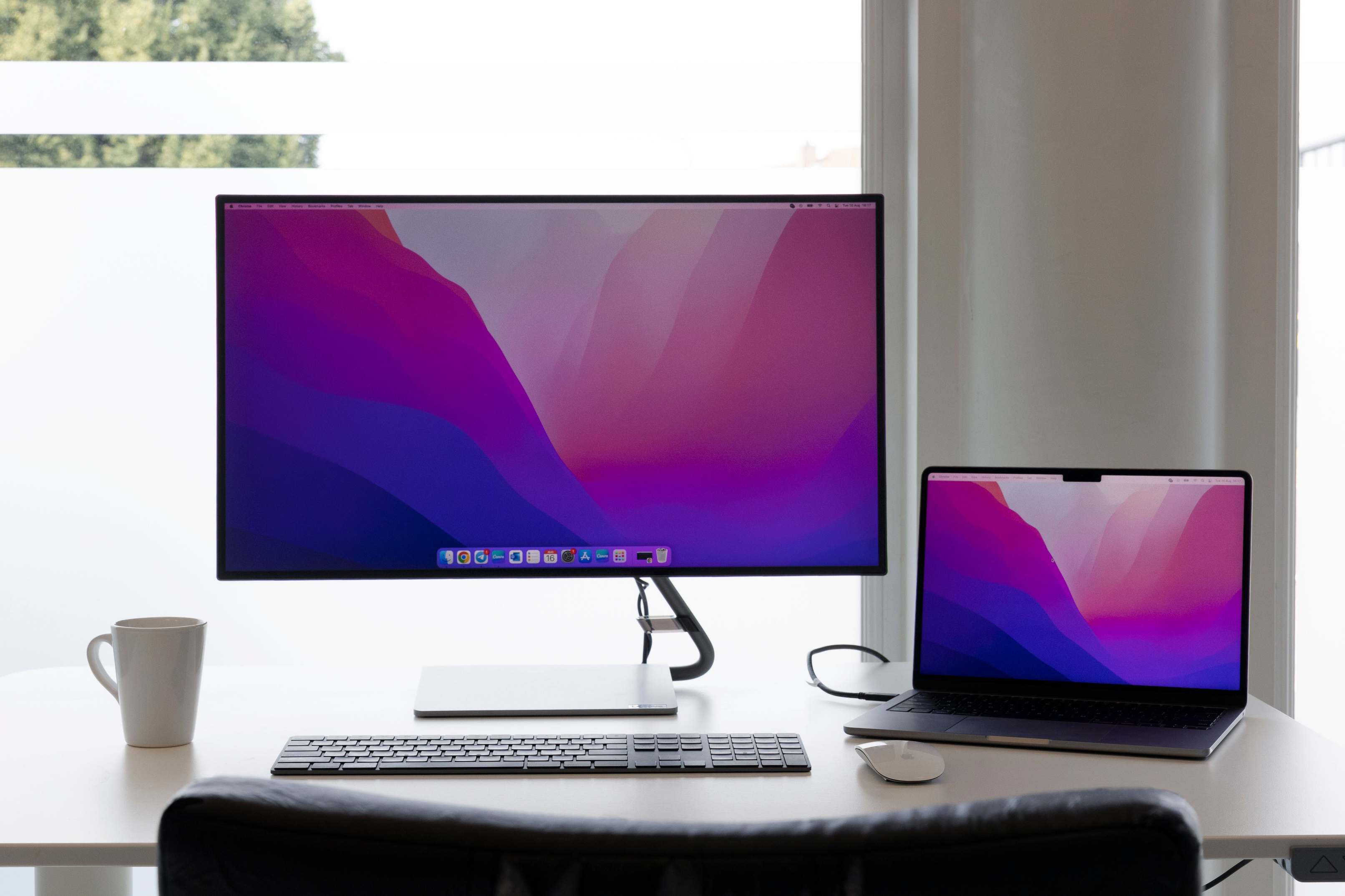 Close-up of a laptop keyboard and screen in a workspace with dual monitors